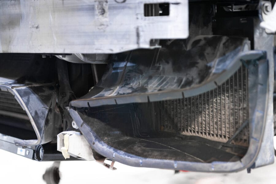 Close-up underside view of a BMW F82 M4's auxiliary cooler duct and radiator core, showing a duct tape repair holding the plastic shroud in place.