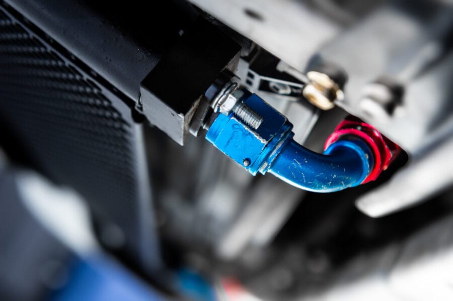 Close-up of blue and red anodized AN fittings from ColorFittings connecting a custom oil cooler line to a CSF cooler on a BMW race build.