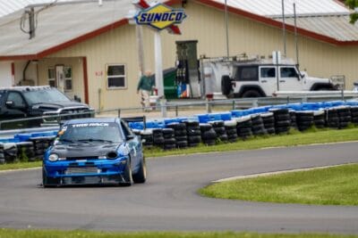 Blue 1999 Dodge Neon driving through a track corner with a low front splitter and rear wing