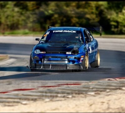 1999 Dodge Neon cornering on track with its front splitter and support rods loaded