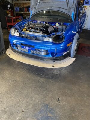 Front view of a blue 1999 Dodge Neon with a half-inch plywood splitter and four splitter support rods