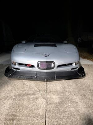 Front view of a silver 2000 Chevrolet Corvette C5 with a homemade carbon splitter and Professional Awesome support rods