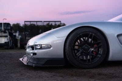 Low side profile of Justin Crews’ silver C5 Corvette showing the carbon splitter, quick-release mounts, and support rod