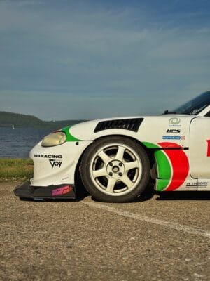Side profile of a white 2000 Mazda Miata NB showing its front splitter, support rod, and titanium skid block