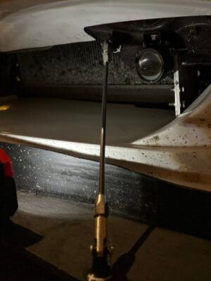 Close-up of a splitter support rod attached at a factory crash-bar mounting point behind the bumper of a 2000 Mazda Miata NB