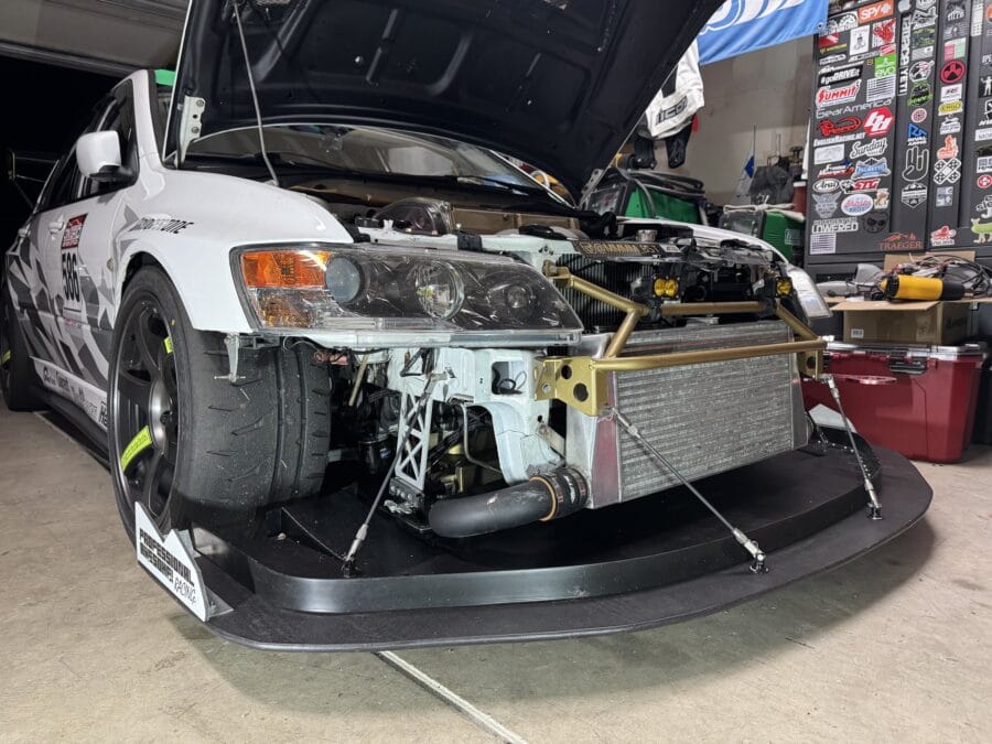Front bumper removed from a white 2005 Mitsubishi Evo 8 to show the quick-release splitter support system and support rods