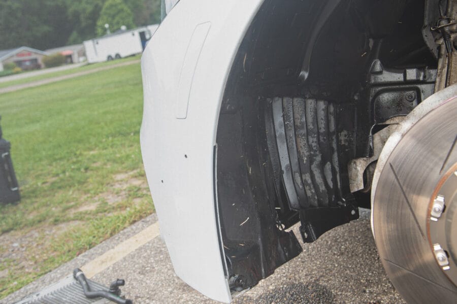 Close-up of a BMW F82 M4's wheel well with coolant visibly leaking down the black fender liner, brake rotor and radiator hose visible nearby.