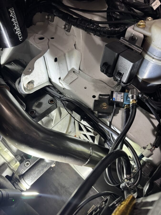 Engine-bay detail of the bolts used to mount a splitter support system through a Mitsubishi Evo 8 frame rail