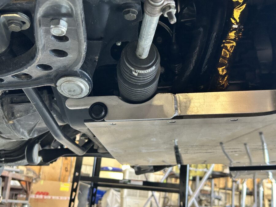 Fabricated splitter support bracket and aluminum panel beside the steering rack boot under Drew’s BMW E30.