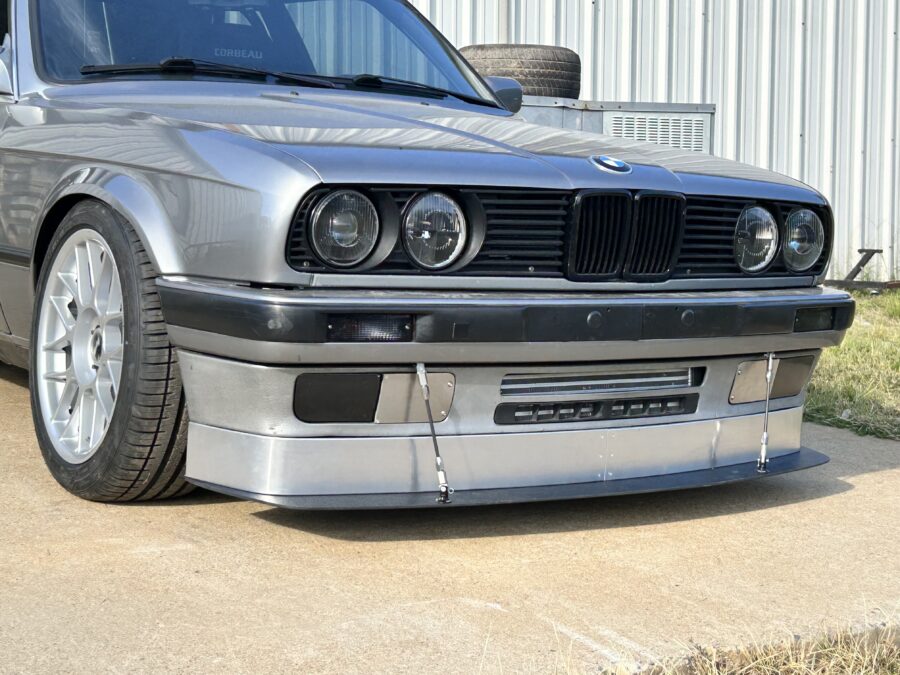 Front three-quarter view of Drew Fuller’s silver 1989 BMW E30 325is with ABS splitter, aluminum air dam, and two support rods.