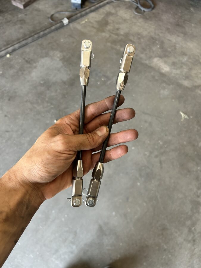 Pair of assembled Professional Awesome splitter support rods with clevises, pins, and retaining clips held before installation.