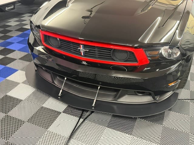 Three-quarter front view of a black and red Boss 302 Laguna Seca with two splitter support rods installed.