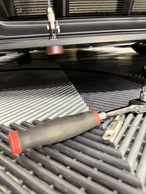Underside view of the splitter support mounting puck on Jon’s Boss 302, with tools beneath the car.